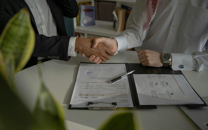 Two people shaking hands over signed paperwork